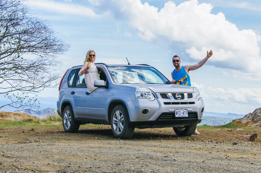 Couple standing with their rental car at a view point showing that it is safe to travel in Costa Rica.