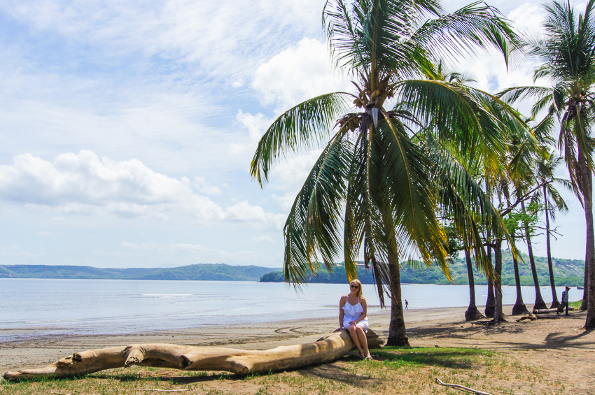 Madison sitting on a log under a palm tree at the beach in Guanacaste, Costa Rica